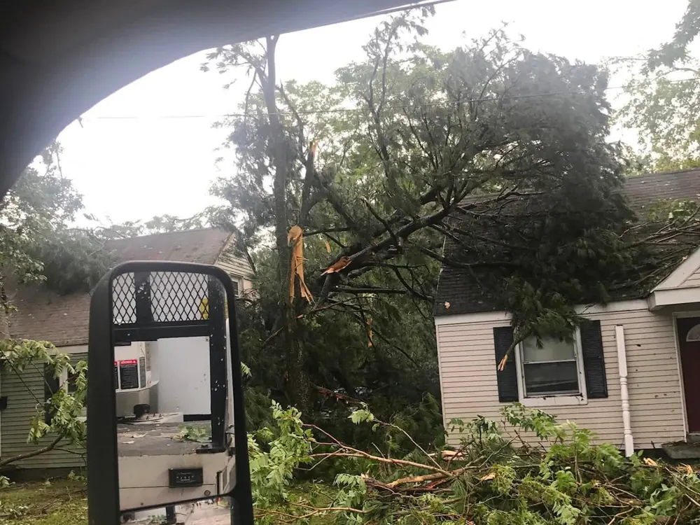 Storm-damaged tree fallen across a home being cleared